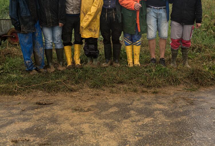Viele Menschen stehen nebeneinander auf dem Feld. Im Fokus des Bildes sind ihre Gummistiefel
