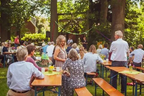 Menschen auf dem Bauckhof Amelinghausen feiern ein Fest. Menschen auf Bierbänken essen, trinken und unterhalten sich.